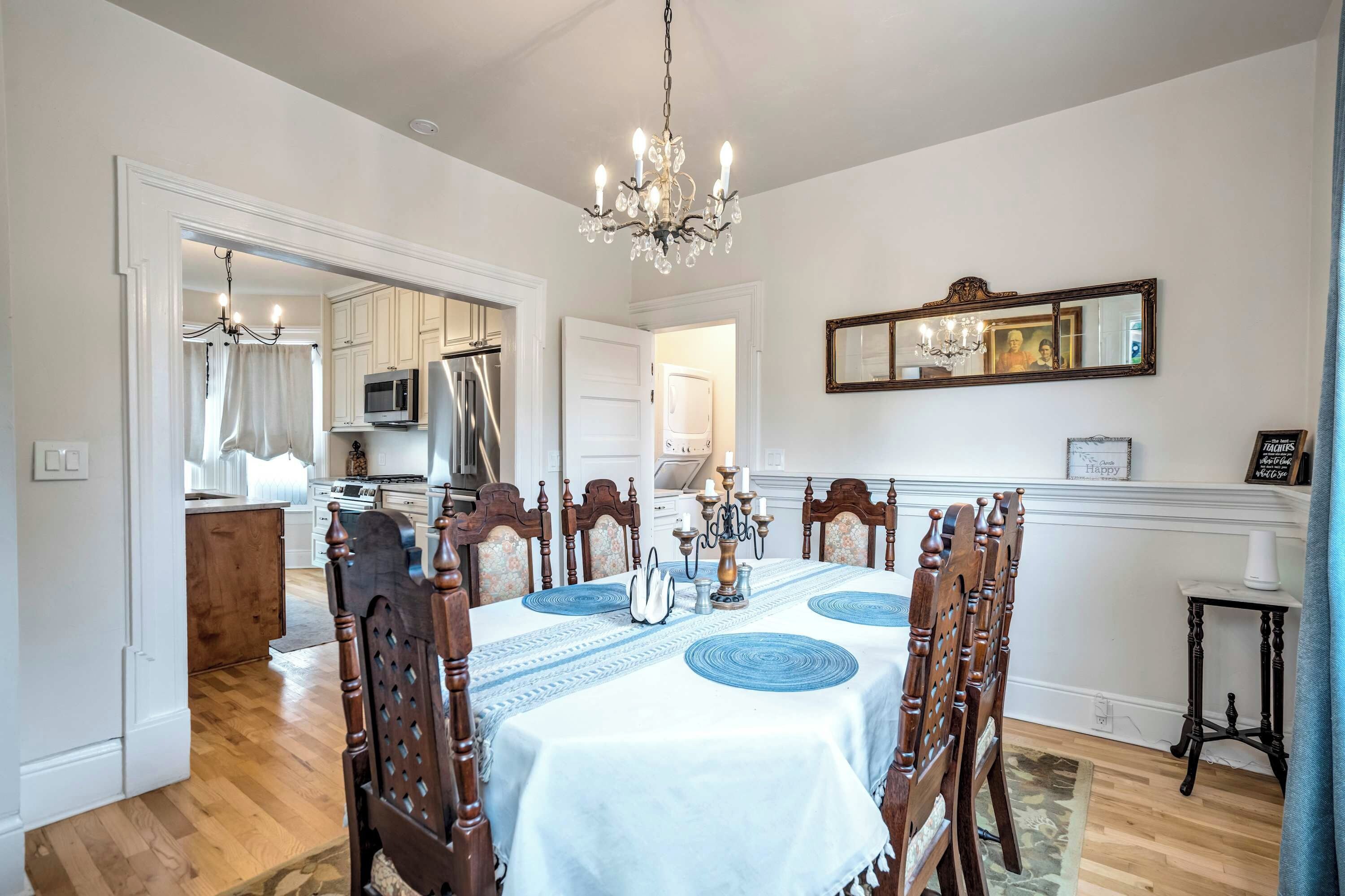 A dining room with a chandelier, a table set for six, and a kitchen in the background.