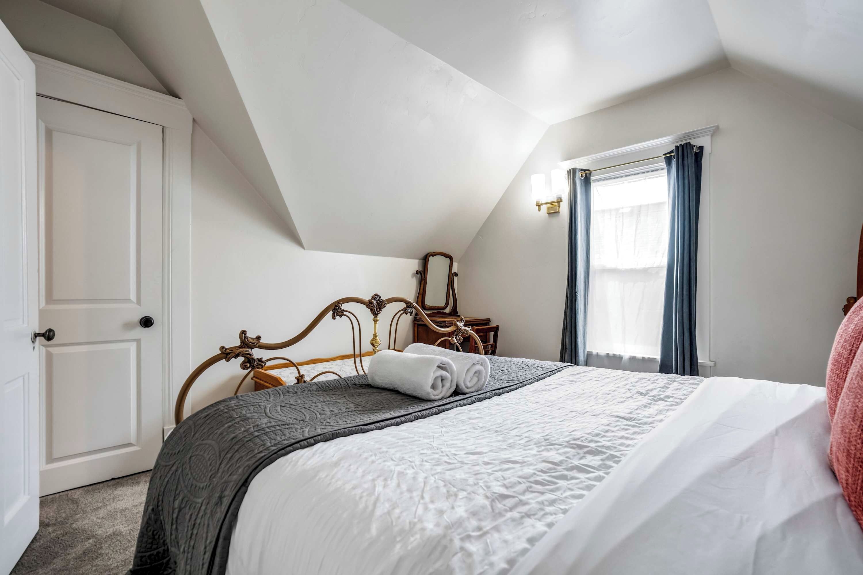 A bedroom with a bed, a door, a window with curtains, and a nightstand.