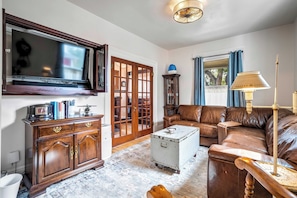 A living room with a television, a wooden cabinet, a leather sofa, a patterned rug, and a decorative lamp. - Chestnut Hill! Downtown Historic Home w Hot Tub (Colorado Springs)