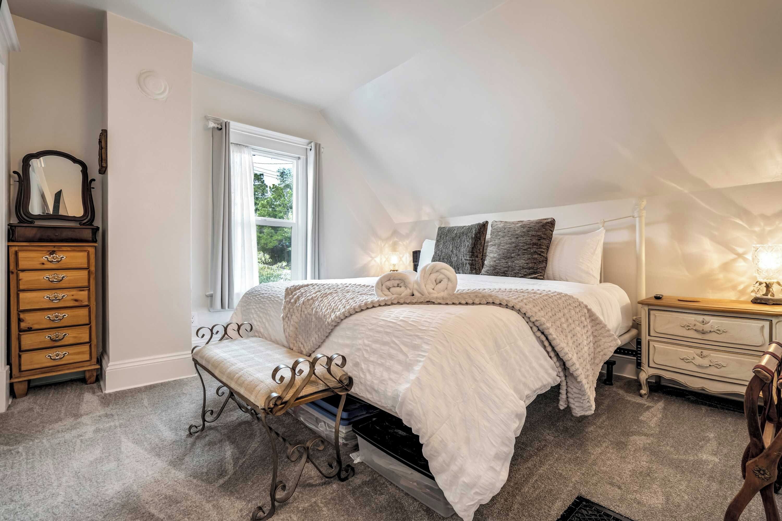 A bedroom with a bed, bedside tables, a bench, a dresser, and a window.