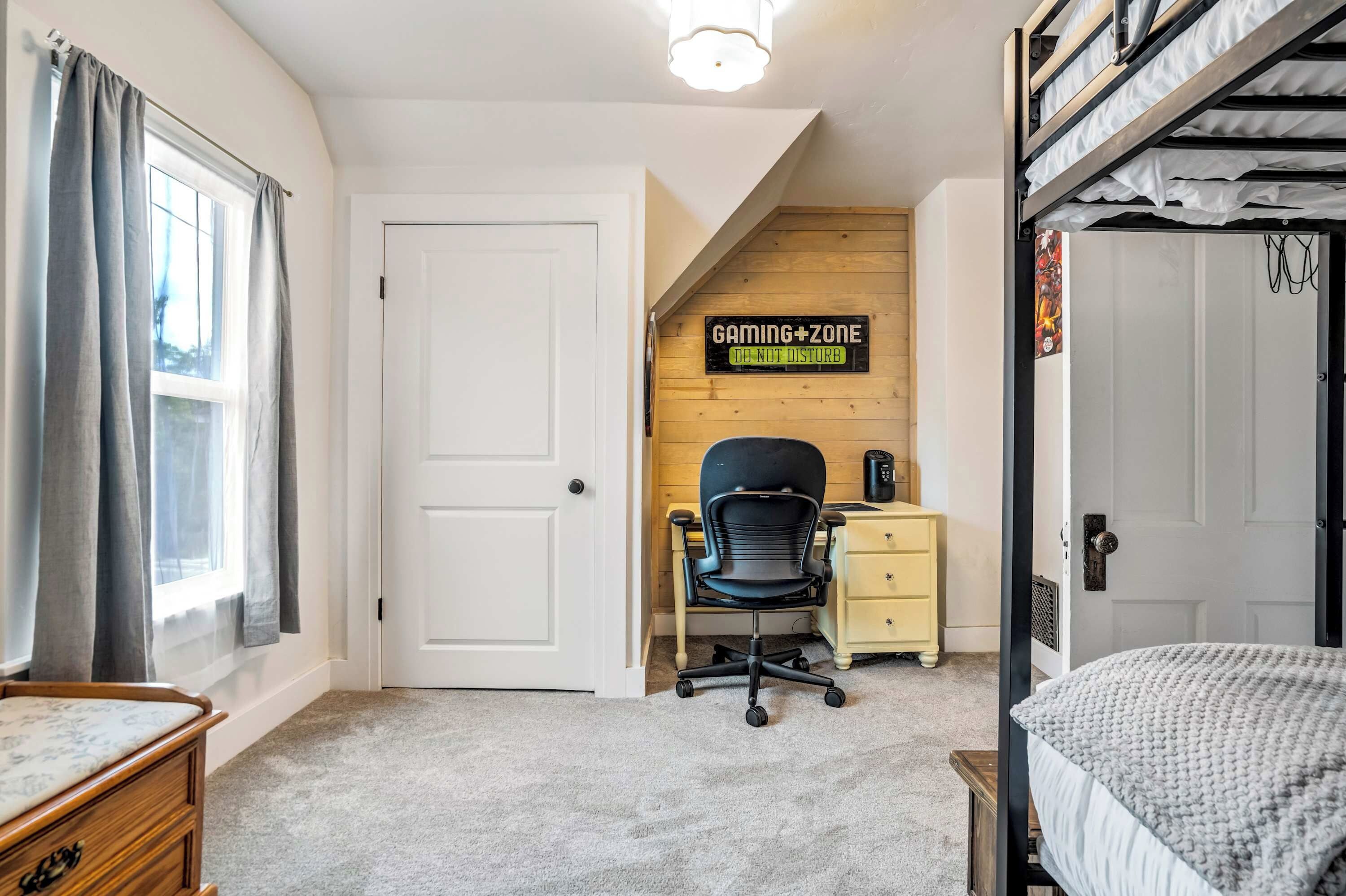 A room with bunk beds, a desk with a chair, a 'Gaming Zone' sign, a window with curtains, and a door.