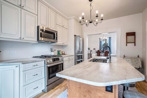 A kitchen with white cabinetry, a central island, stainless steel appliances, and a chandelier. - Chestnut Hill! Downtown Historic Home w Hot Tub (Colorado Springs)