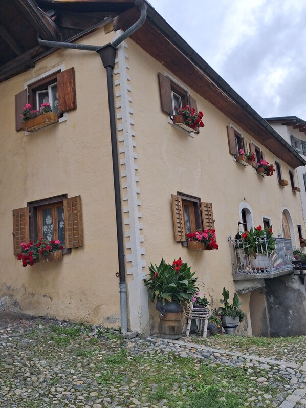 Ein Gebäude mit zahlreichen Fenstern, von denen einige mit Fensterläden versehen sind, und Blumenkästen an der Außenfassade.