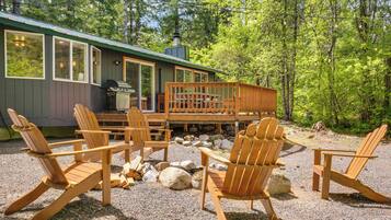 A cabin with a deck, outdoor seating, and a grill.