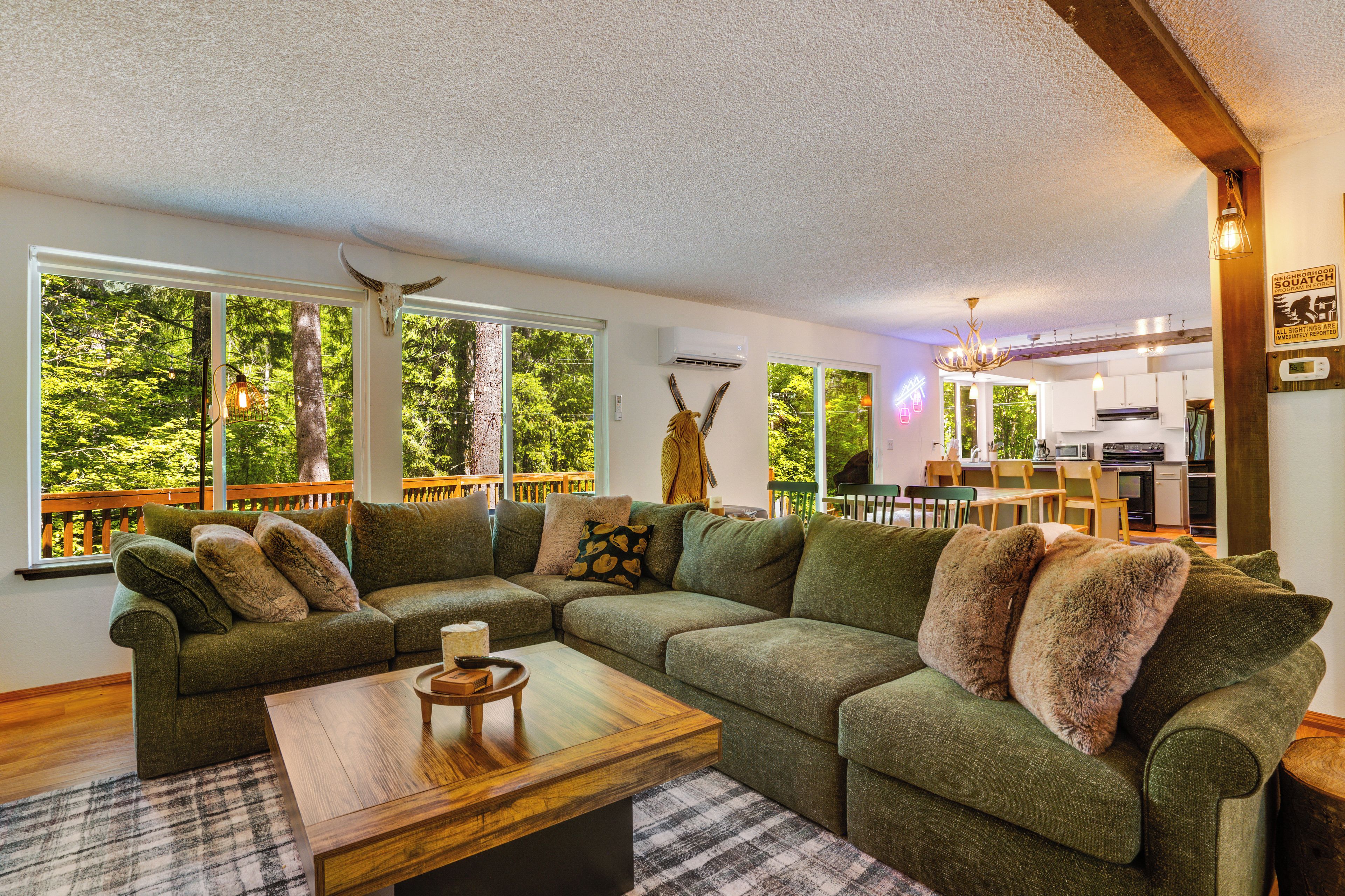 A cozy living room with a sectional sofa, a wooden coffee table, and a view of the outdoors through large windows.
