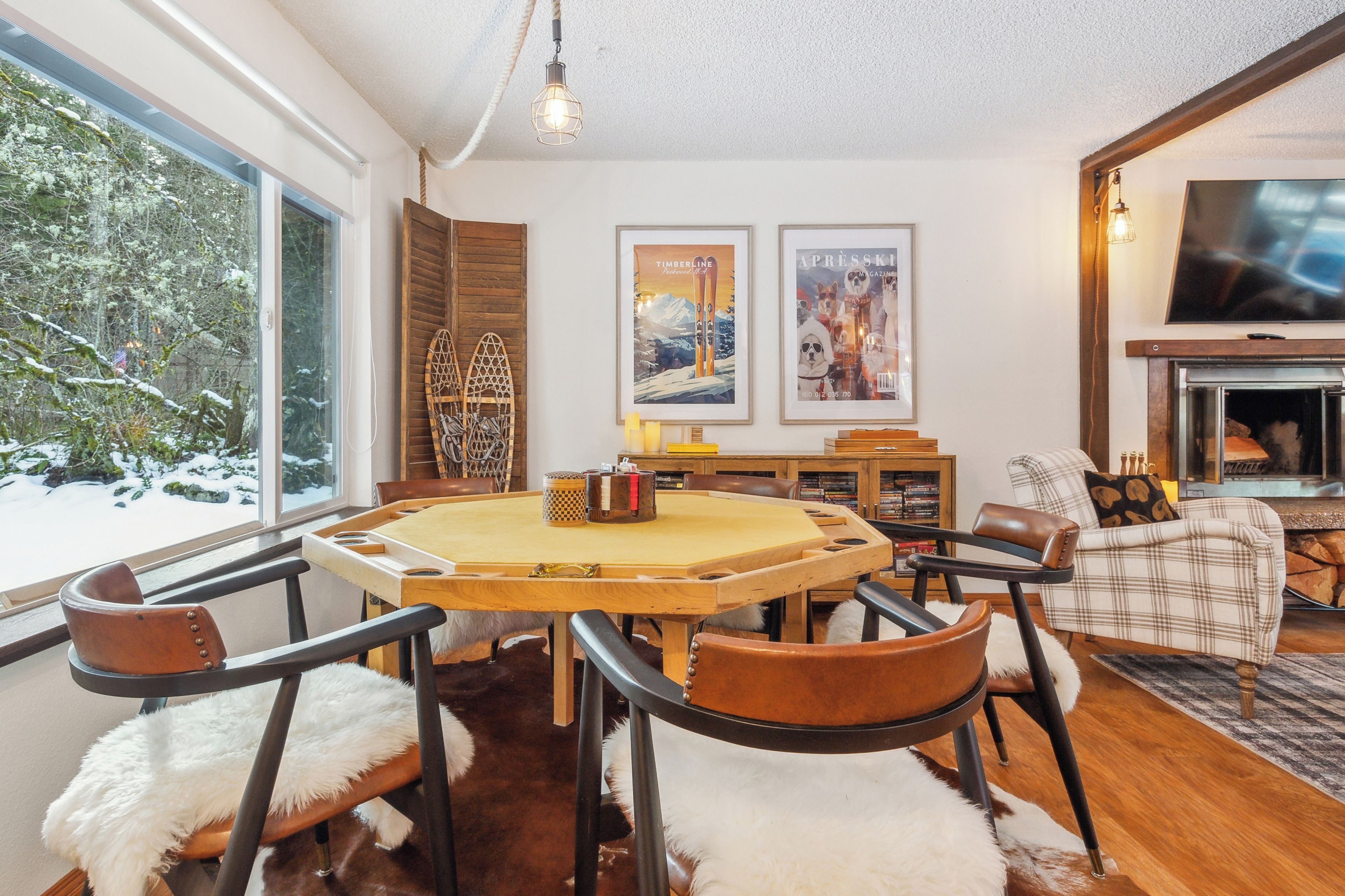 A cozy living room with a fireplace, a dining table with chairs, and a large window overlooking a snowy landscape.