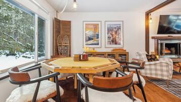 A cozy living room with a fireplace, a dining table with chairs, and a large window overlooking a snowy landscape.