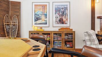 Ein gemütliches Zimmer mit einem Holztisch, einem Ledersessel und einem Bücherregal voller Gesellschaftsspiele.