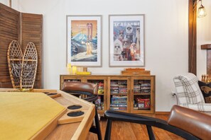 Une pièce chaleureuse avec une table à manger en bois, un fauteuil en cuir et une bibliothèque remplie de jeux de société.