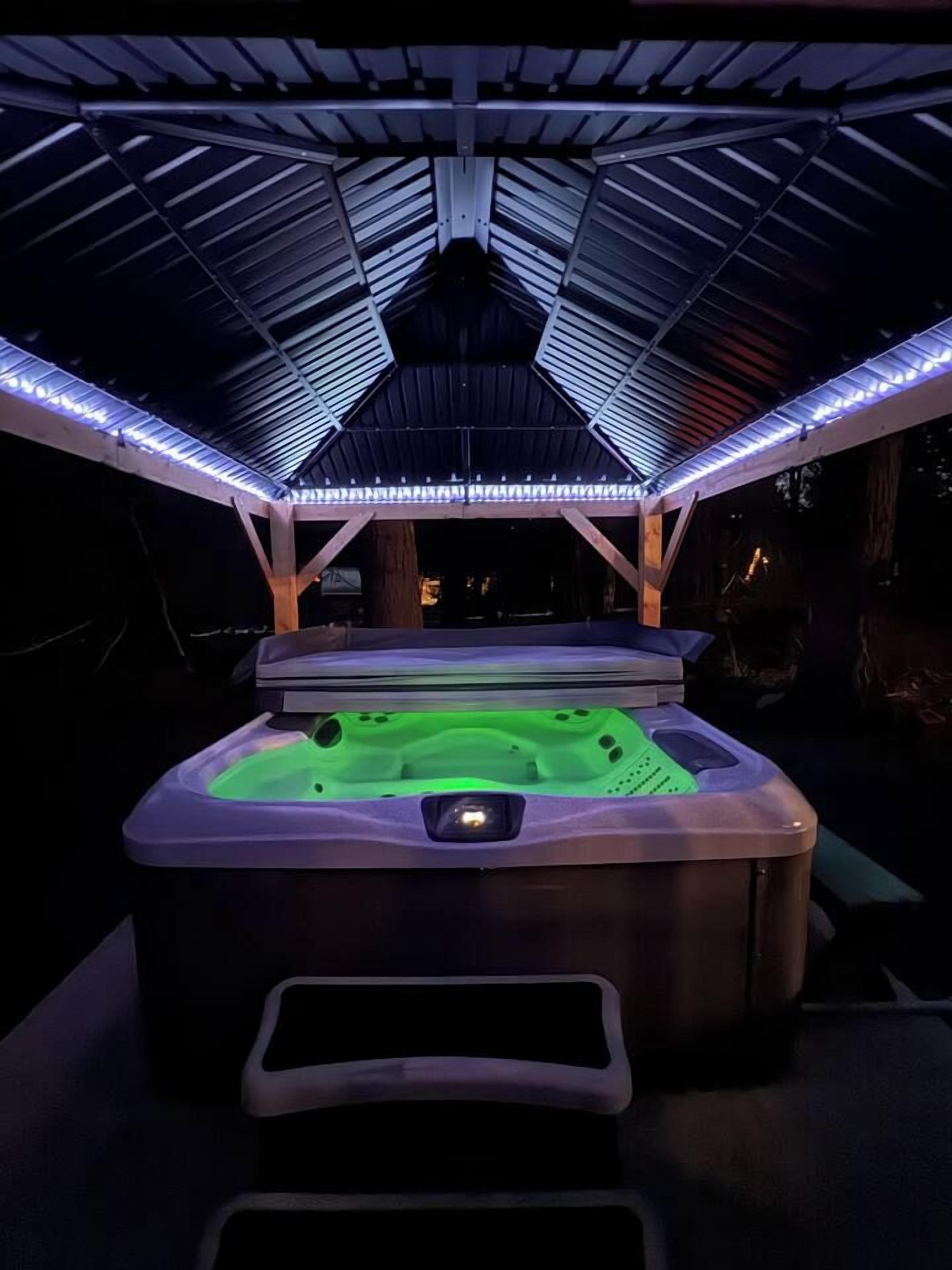 A hot tub under a covered area with a roof structure and LED lighting.