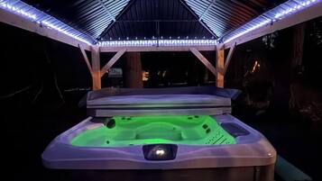 A hot tub under a covered area with a roof structure and LED lighting.