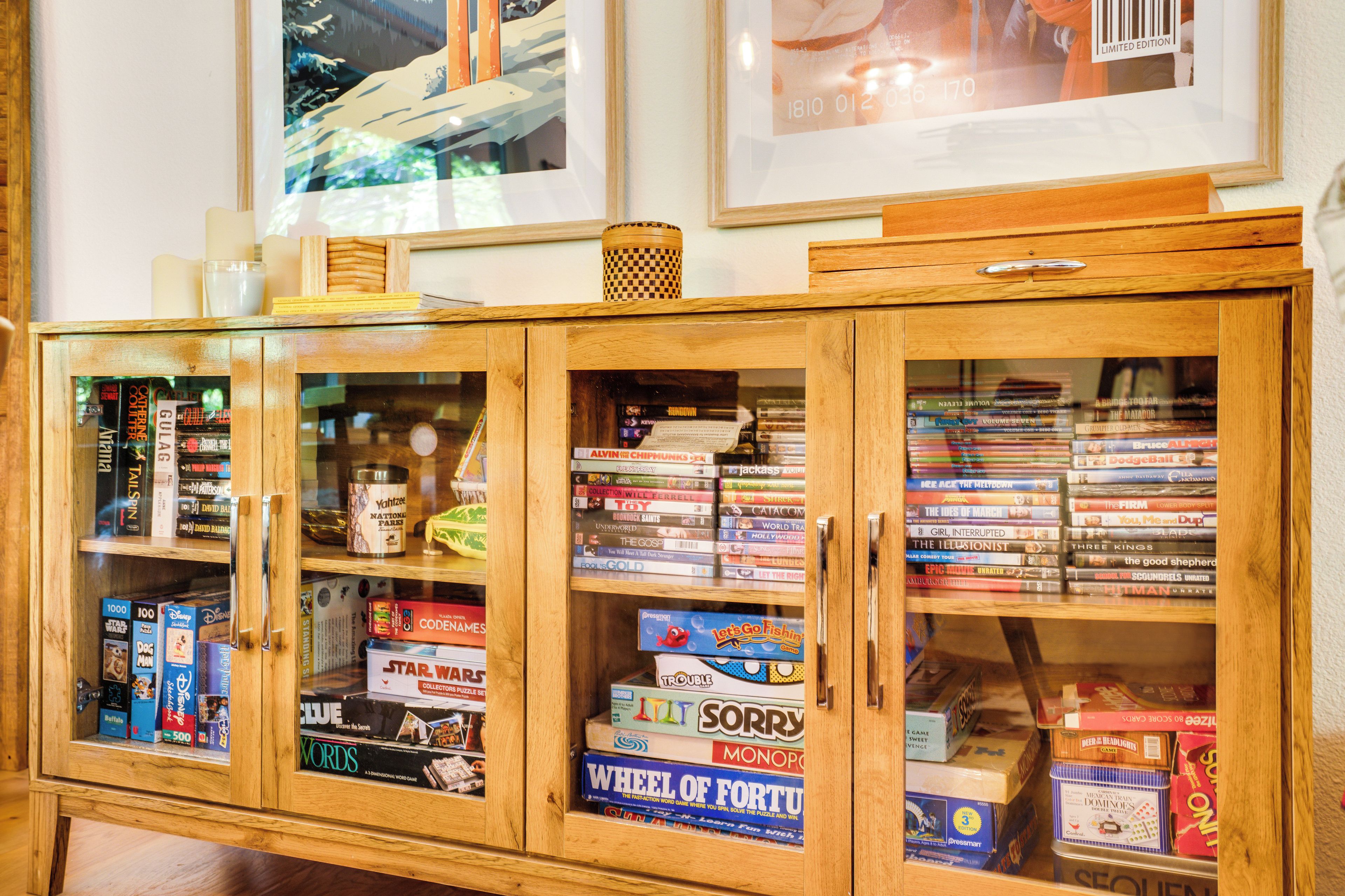 A wooden cabinet with glass doors displaying various board games and puzzles.