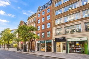 A street view with a row of buildings, including a pharmacy, a clinic, and a store with a green sign. - City Double VIII - 2BR home with terrace in the City (London)