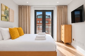 A hotel room with a bed, a wooden dresser, a flat-screen TV, and a view of buildings through the door. - City Double IX - Stylish 2BR home in the City (London)