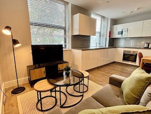 A modern living room with a flat-screen TV, a glass-top coffee table, and a sofa. - City Tower - Stylish 1BR home in the City (London)