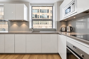 Een moderne keuken met witte kasten, een roestvrijstalen afzuigkap, een ingebouwde magnetron en een raam met jaloezieën.