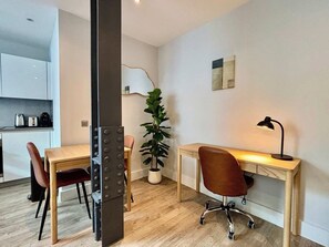A modern kitchen with white cabinets, a dining table with chairs, a potted plant, and a desk with a lamp. - City Tower - Stylish 1BR home in the City (London)