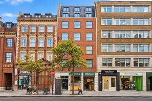 Une rangée d’immeubles à étages, avec différentes boutiques en rez-de-chaussée, notamment une pharmacie, une clinique et un restaurant.