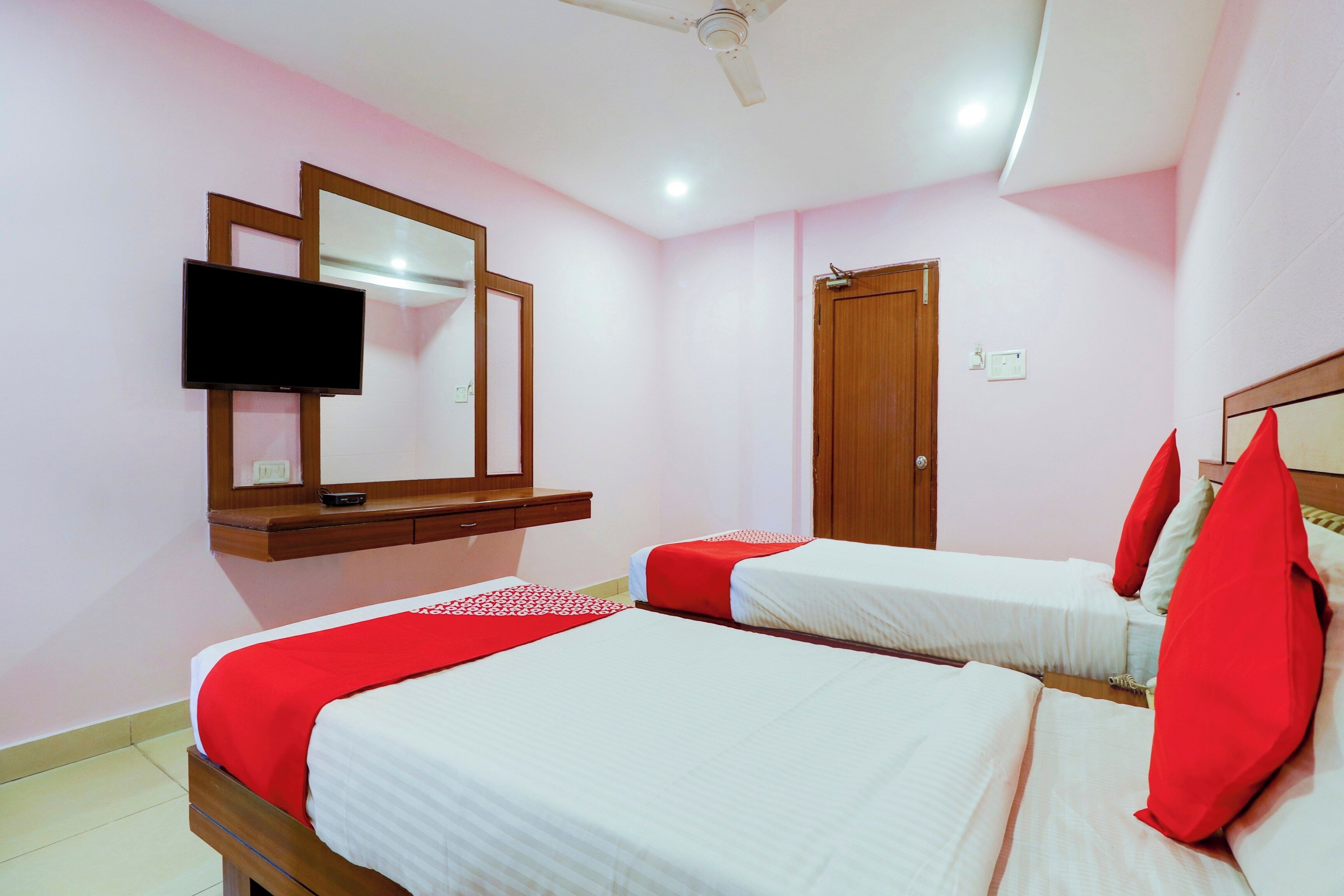 A hotel room with two beds, a television mounted on the wall, a ceiling fan, and a door.