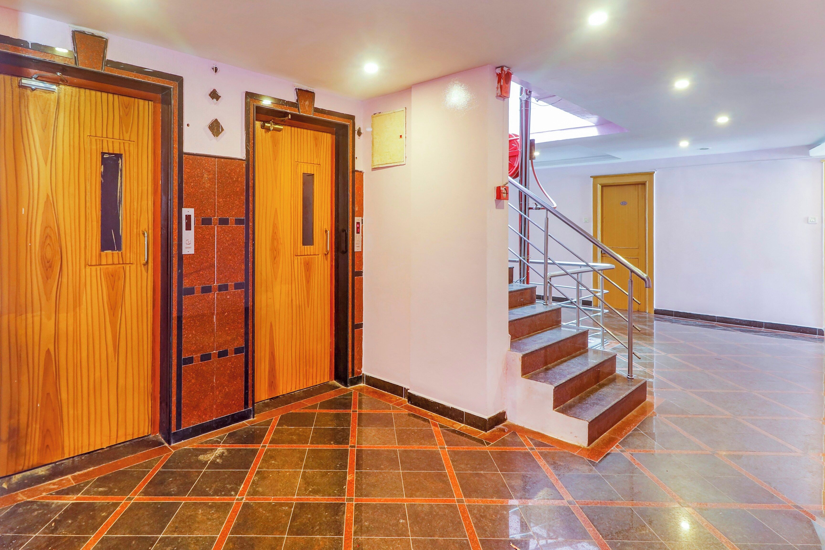 A hotel lobby with a wooden elevator, a staircase, and a tiled floor.