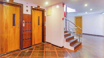 A hotel lobby with a wooden elevator, a staircase, and a tiled floor.