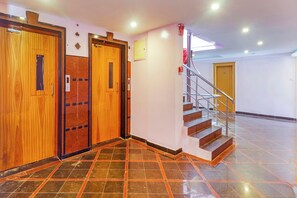 A hotel lobby with a wooden elevator, a staircase, and a tiled floor. - Hotel O Vaishnavi Palace (Hyderabad)