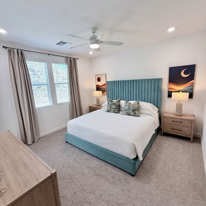 Quarto com cama, cortinas, ventoinha no teto e obras de arte nas paredes.