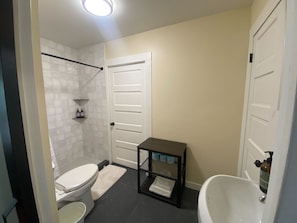 Un baño con inodoro, ducha, lavabo y un pequeño estante con artículos de aseo.