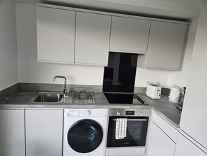 A compact kitchen with a washing machine, a built-in oven, a sink, and a toaster. -  Beautiful  modern 2 bed flat in Manchester close to Media City/Old Trafford  (Salford)