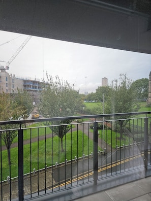 Udsigt fra en balkon over et byggeplads med en kran, en bygning i opførelse og et grønt parkområde.
