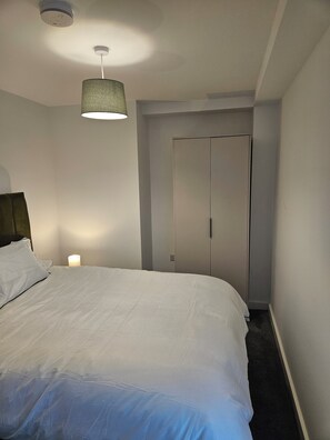A bedroom with a bed, a bedside lamp, a ceiling light fixture, and a wardrobe. -  Beautiful  modern 2 bed flat in Manchester close to Media City/Old Trafford  (Salford)