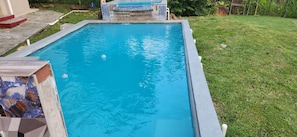 A rectangular swimming pool with a clear blue water surface, surrounded by a grassy area and a tiled deck. - Castleview villa (Signal Hill)