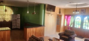 A room with a wooden bar area, a seating area with a patterned armchair, and a television mounted on the wall. - Castleview villa (Signal Hill)