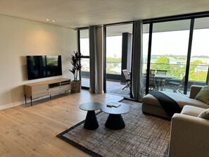 Ein modernes Wohnzimmer mit Fernseher, einer Couch, zwei Couchtischen und einem Balkon mit Blick.