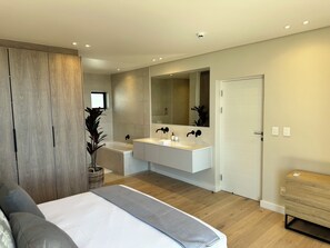 Un dormitorio moderno con una cama grande, un tocador integrado y una zona de ducha separada.