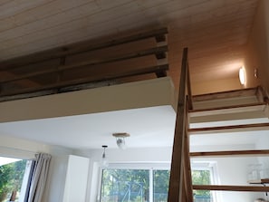 Una habitación con techo de madera, pared blanca y ventana con vista a la vegetación.