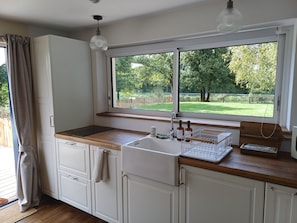 Eine Küche mit Fenster, Holz Arbeitsplatte, weißen Schränken und einer Hängeleuchte.
