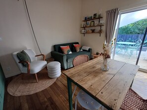 Uma sala de estar aconchegante com uma mesa de jantar de madeira, um sofá verde e uma cadeira de vime.