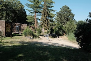 A fenced outdoor area with a grassy lawn, trees, and a building with a door. - kleiner Heidesee (Versmold)