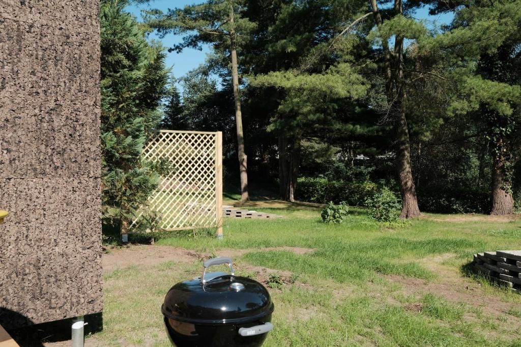 An outdoor grill with a lid, surrounded by a grassy area and trees.