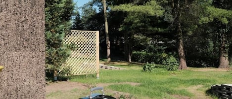 An outdoor grill with a lid, surrounded by a grassy area and trees.