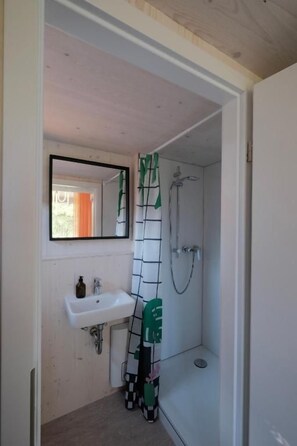 A bathroom with a white sink, a mirror, and a shower. - kleiner Heidesee (Versmold)