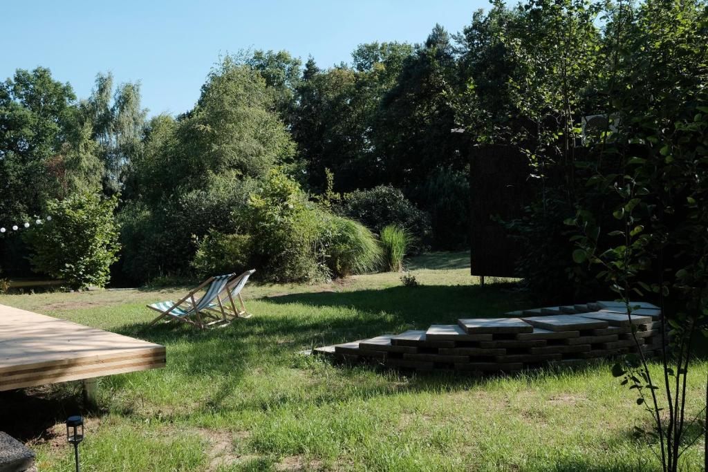 Een houten terras met een loungeset en een vuurkorf van steen in een gazon met bomen.