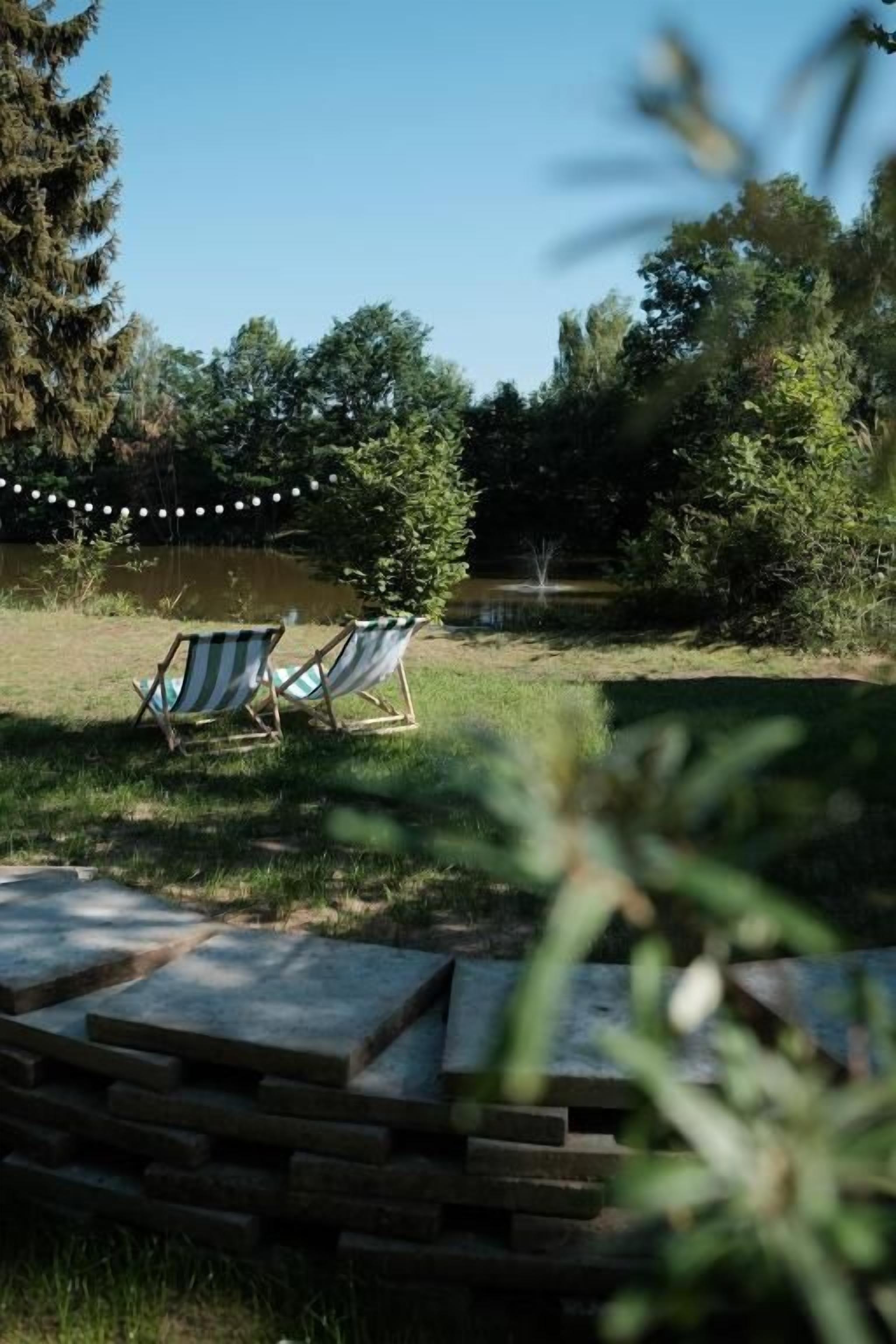 Nurmikkoalue ulkona, jossa on kaksi raidallista aurinkotuolia ja kivipolku, joka johtaa vesistöön.
