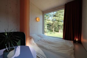 Un dormitorio con cama, ventana con cortinas, una planta en maceta y una lámpara de pared.