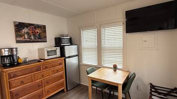 Une cuisine compacte équipée d’un four à micro-ondes, d’un réfrigérateur et d’une commode en bois. On y trouve une table à manger avec des chaises, ainsi qu’un tableau accroché au mur.