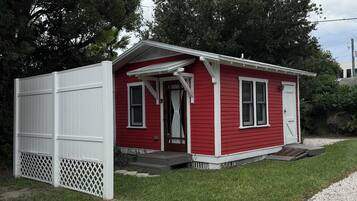Une petite maison rouge à un seul étage, avec un porche blanc et une clôture blanche.