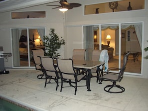 An outdoor patio with a table and chairs, a ceiling fan, and a view into the house through glass doors. - Luxury 3 Bedroom Villa (Rotonda West)