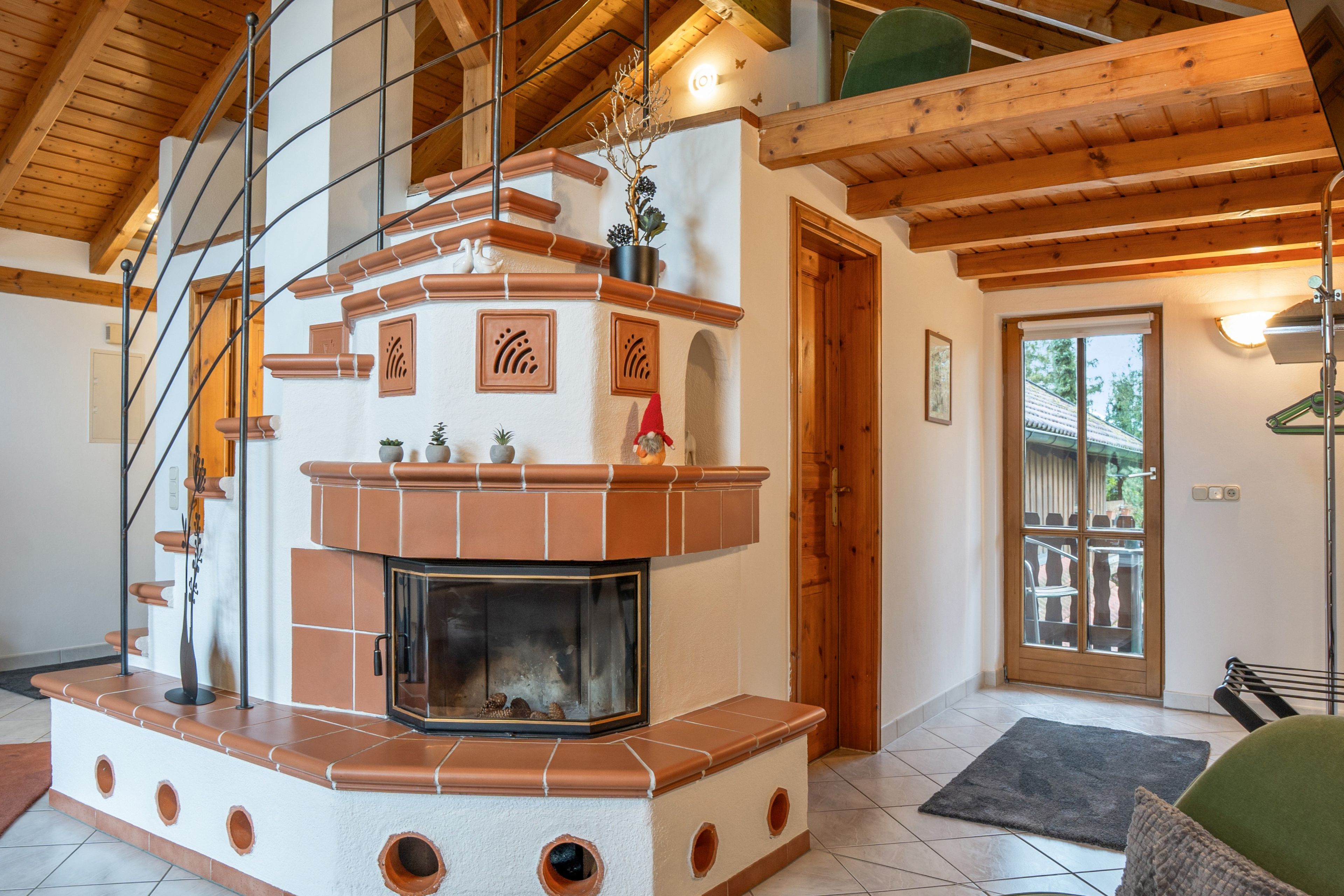 A fireplace with a tiled surround, a wooden ceiling, and a door leading outside.