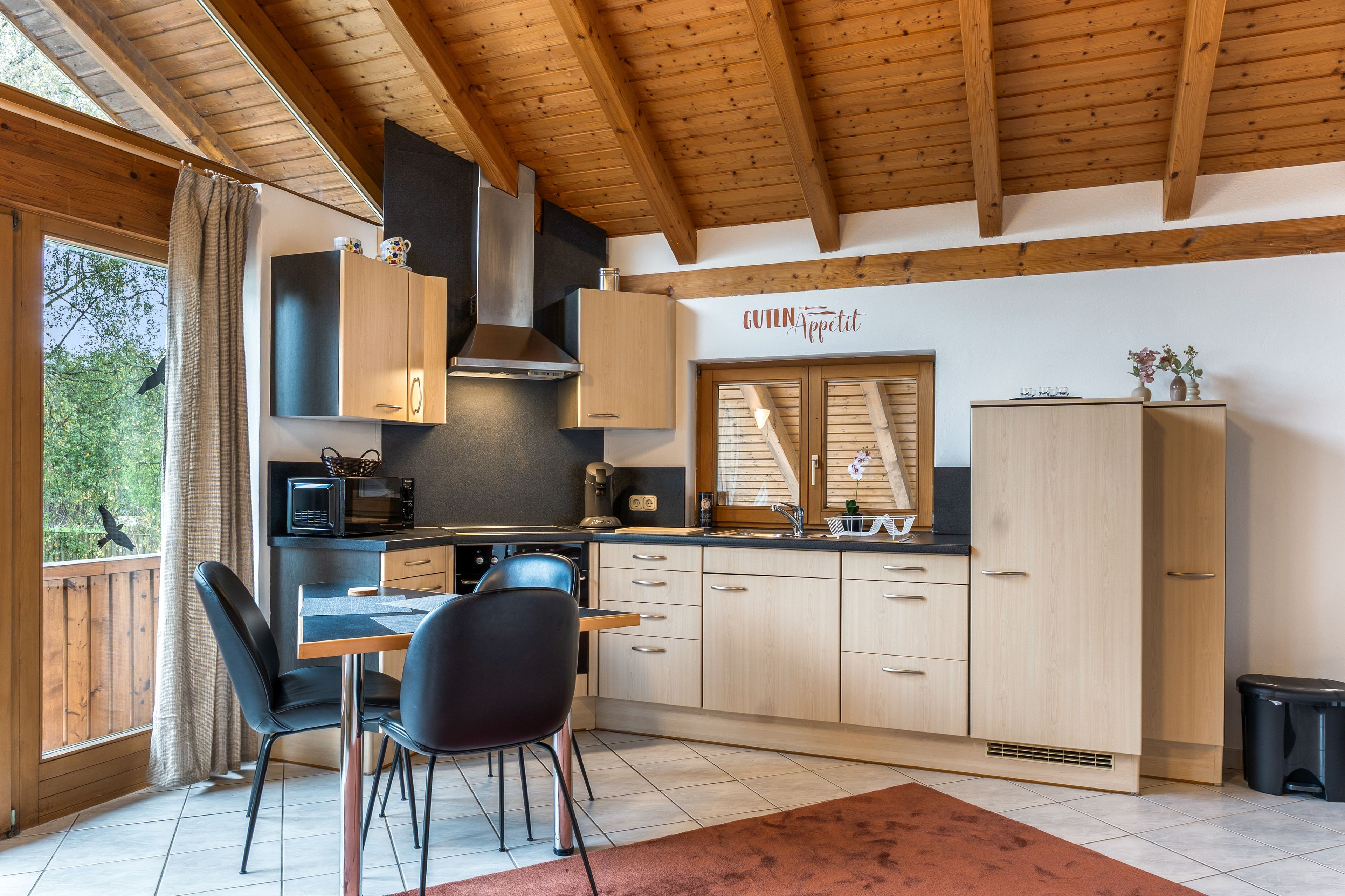 Une cuisine moderne avec des meubles en bois, un coin repas comprenant une table et des chaises, et une vue sur l’extérieur par une fenêtre.